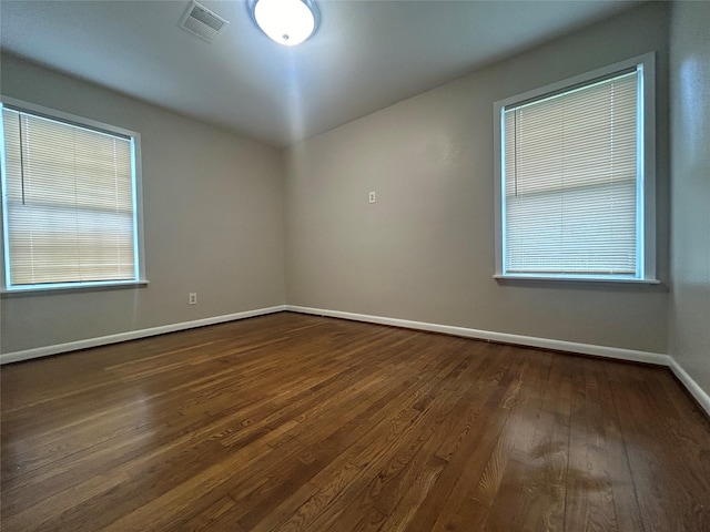 unfurnished room featuring dark wood-style floors, visible vents, and baseboards