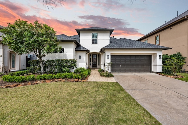 view of front of property featuring roof with shingles, stucco siding, a garage, a yard, and driveway