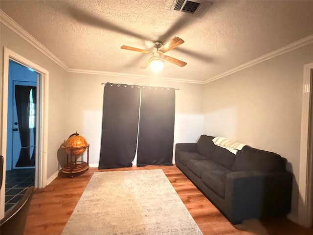 living room featuring visible vents, ceiling fan, ornamental molding, a textured ceiling, and light wood-type flooring