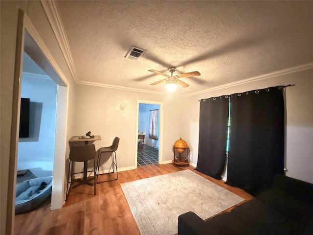 interior space with visible vents, ornamental molding, a textured ceiling, wood finished floors, and ceiling fan