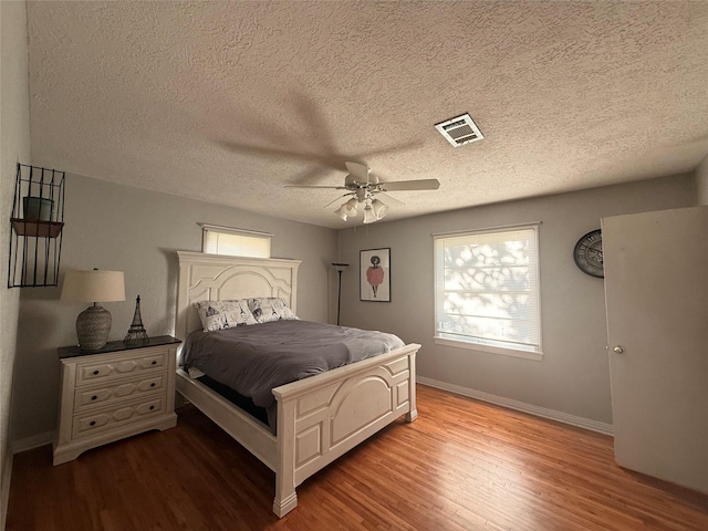 bedroom with wood finished floors, visible vents, baseboards, ceiling fan, and a textured ceiling