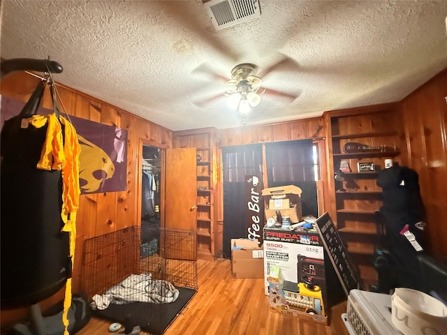 home office with visible vents, wood walls, wood finished floors, a textured ceiling, and a ceiling fan