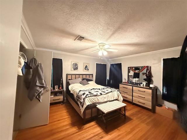 bedroom featuring crown molding, wood finished floors, visible vents, and a textured ceiling