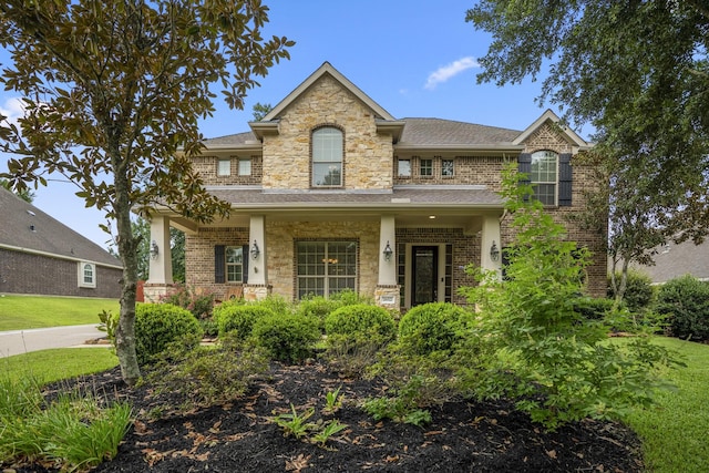 view of front of home with stone siding, brick siding, covered porch, and a front yard