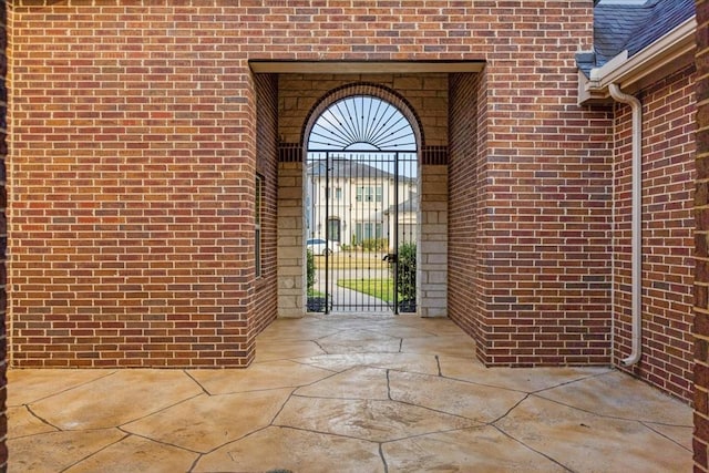 entrance to property with brick siding, roof with shingles, and a gate