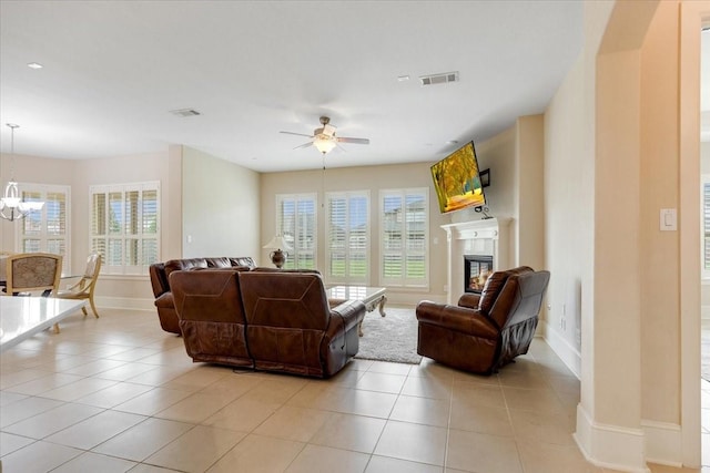 living room featuring visible vents, baseboards, light tile patterned floors, ceiling fan with notable chandelier, and a glass covered fireplace