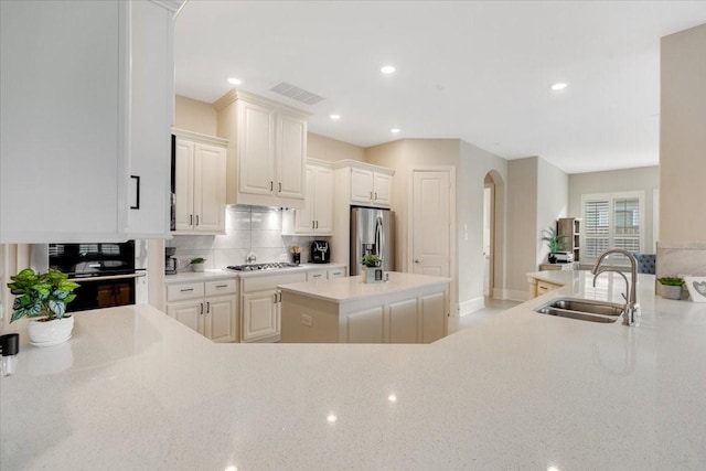 kitchen featuring visible vents, a sink, arched walkways, appliances with stainless steel finishes, and decorative backsplash