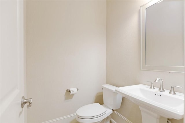 half bath featuring toilet, baseboards, and a sink