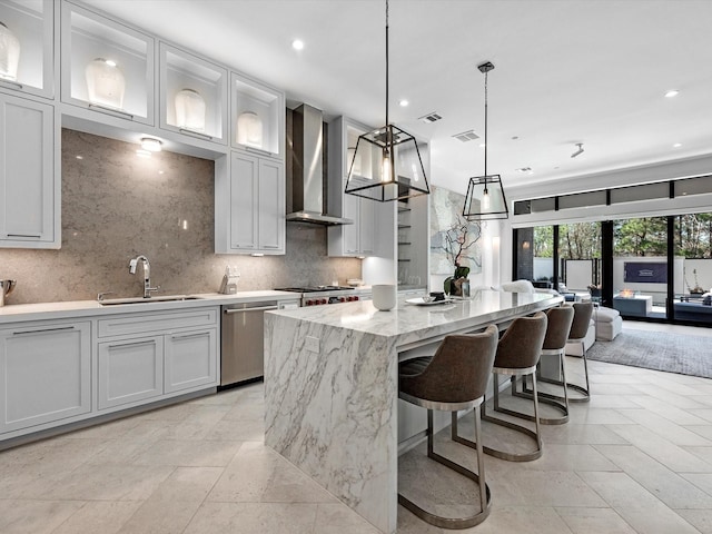 kitchen featuring light stone countertops, a kitchen island, a sink, appliances with stainless steel finishes, and wall chimney range hood