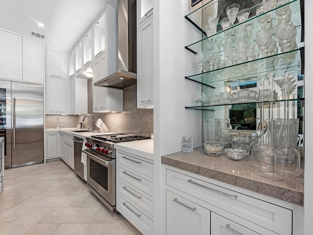 kitchen with visible vents, high quality appliances, white cabinets, wall chimney exhaust hood, and tasteful backsplash