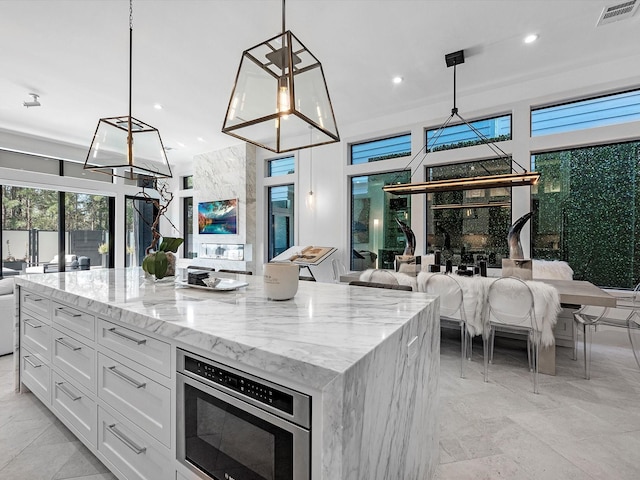 kitchen with light stone counters, visible vents, recessed lighting, white cabinets, and a center island