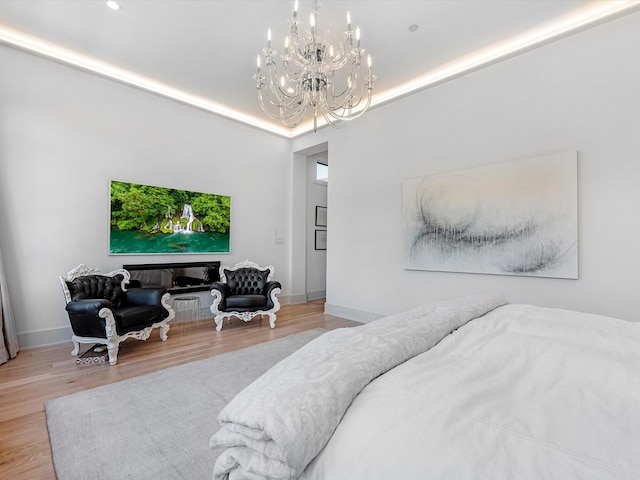 bedroom featuring a tray ceiling, baseboards, an inviting chandelier, and wood finished floors