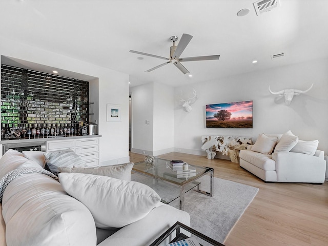 living area featuring visible vents, a bar, light wood-type flooring, and ceiling fan