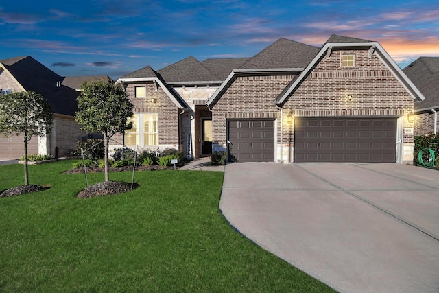 view of front of house featuring brick siding, a shingled roof, a yard, a garage, and driveway