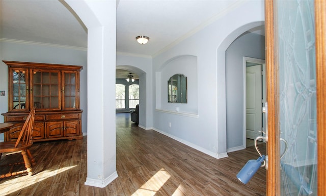 interior space featuring arched walkways, dark wood finished floors, crown molding, and baseboards