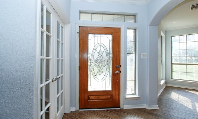 foyer featuring dark wood finished floors, a healthy amount of sunlight, arched walkways, and ornamental molding