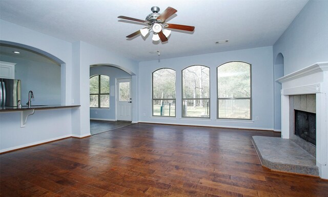 unfurnished living room with a tiled fireplace, baseboards, and dark wood-style flooring