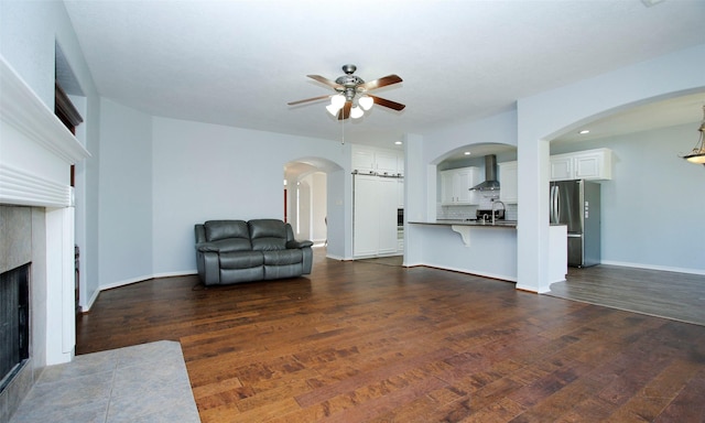 living room with dark wood-type flooring, a fireplace with flush hearth, baseboards, and ceiling fan