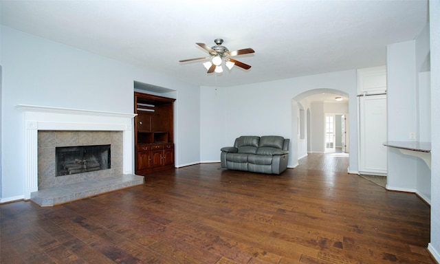 unfurnished living room featuring hardwood / wood-style floors, baseboards, arched walkways, and a tile fireplace