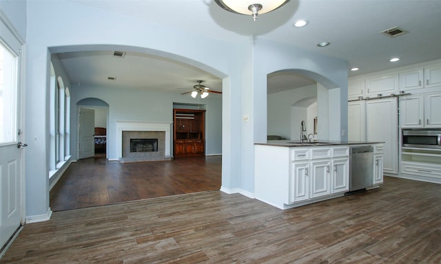 kitchen with dark wood-type flooring, a fireplace with raised hearth, a sink, white cabinetry, and appliances with stainless steel finishes