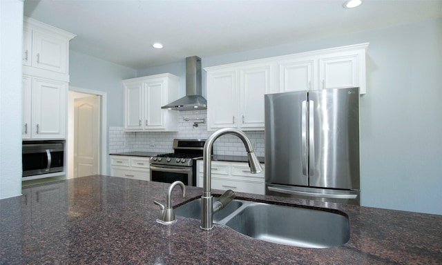 kitchen featuring decorative backsplash, appliances with stainless steel finishes, white cabinets, wall chimney exhaust hood, and a sink