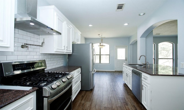 kitchen featuring visible vents, white cabinets, stainless steel appliances, wall chimney exhaust hood, and a sink