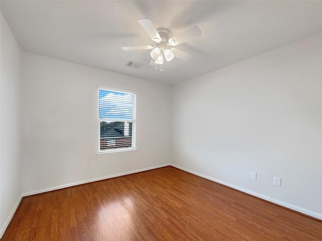 empty room with a ceiling fan, wood finished floors, visible vents, and baseboards