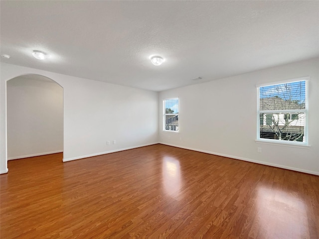 unfurnished room featuring arched walkways, baseboards, and wood finished floors