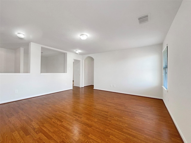 empty room featuring arched walkways, visible vents, baseboards, and wood finished floors