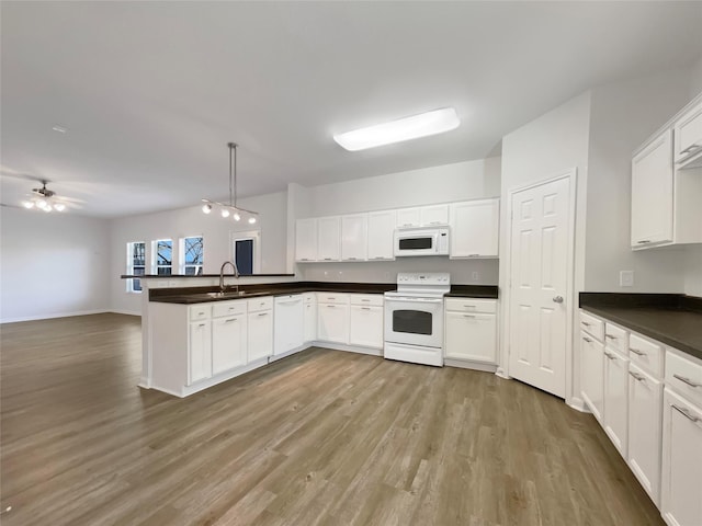 kitchen with dark countertops, light wood-style flooring, a peninsula, white appliances, and a sink