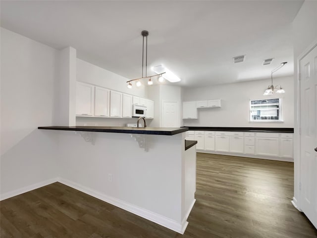 kitchen with visible vents, white microwave, dark countertops, and a peninsula