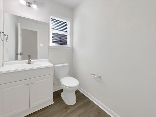 half bathroom featuring toilet, vanity, baseboards, and wood finished floors