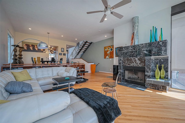 living room featuring recessed lighting, wood finished floors, a fireplace, stairs, and ceiling fan with notable chandelier