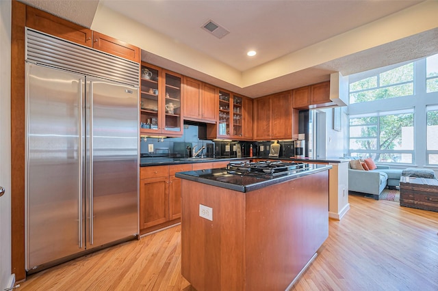 kitchen with light wood finished floors, visible vents, stainless steel built in fridge, brown cabinets, and gas stovetop