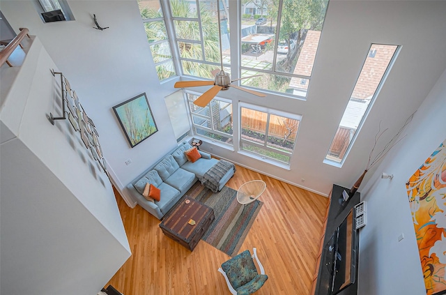 living room featuring ceiling fan, wood finished floors, and a towering ceiling