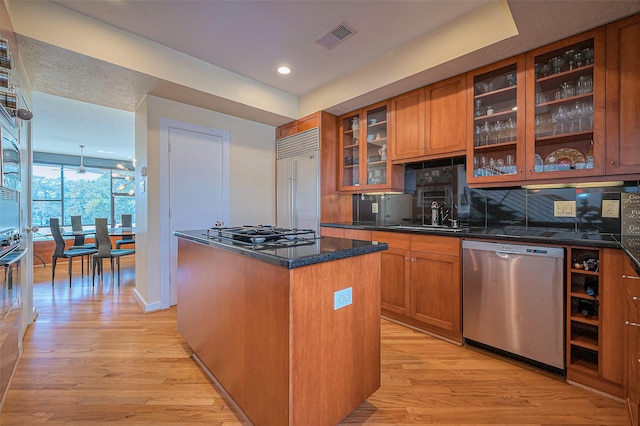 kitchen featuring a sink, tasteful backsplash, stainless steel appliances, brown cabinetry, and light wood finished floors