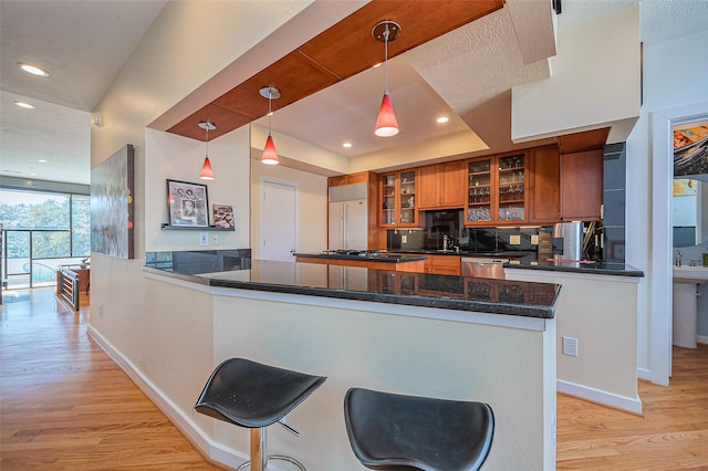 kitchen with a peninsula, stainless steel dishwasher, light wood-type flooring, built in refrigerator, and brown cabinetry