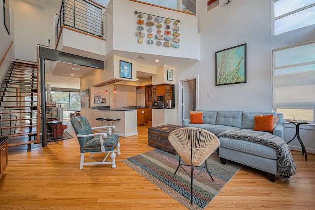 living room featuring light wood-type flooring, visible vents, stairway, baseboards, and a towering ceiling