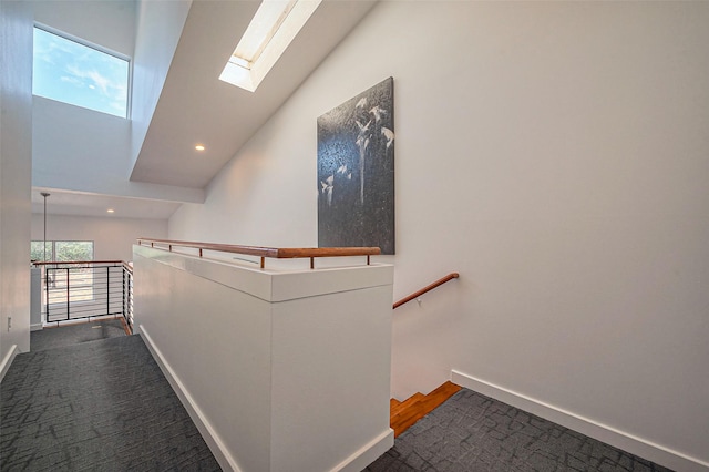 hallway with an upstairs landing, carpet flooring, a skylight, and baseboards