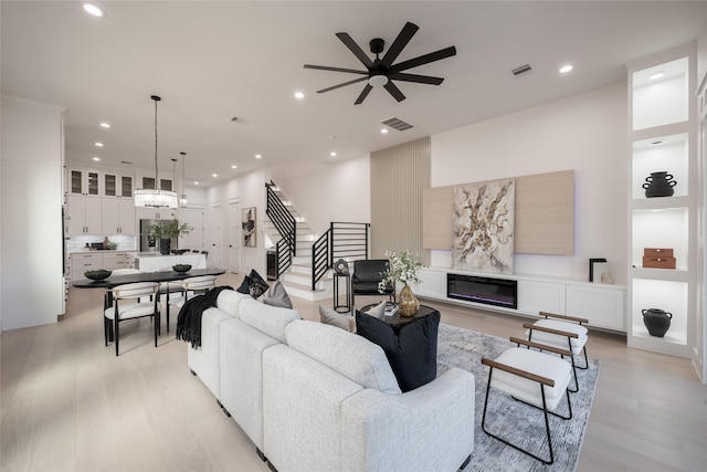 living room with a glass covered fireplace, recessed lighting, stairway, and light wood-type flooring