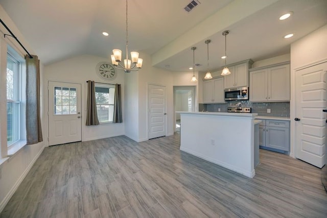 kitchen featuring visible vents, gray cabinets, vaulted ceiling, stainless steel microwave, and tasteful backsplash