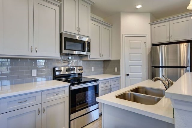 kitchen with backsplash, gray cabinetry, light countertops, stainless steel appliances, and a sink