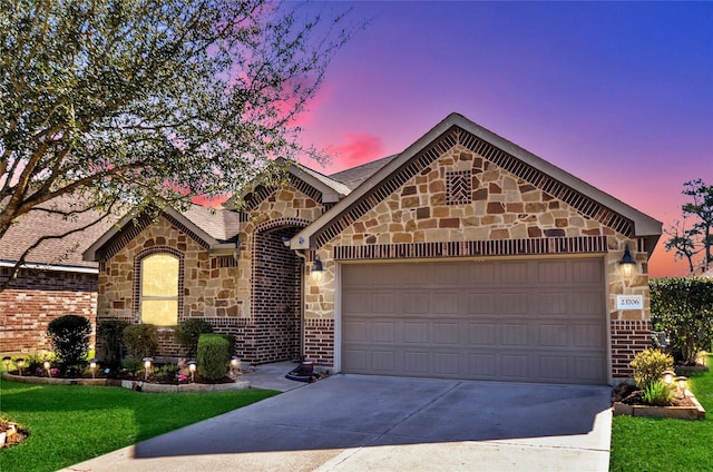 view of front facade with driveway, stone siding, an attached garage, a shingled roof, and brick siding