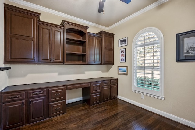 unfurnished office with a ceiling fan, built in desk, crown molding, baseboards, and dark wood-style flooring