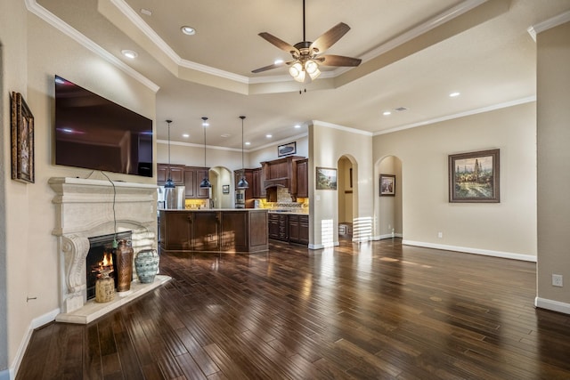 living room with arched walkways, dark wood finished floors, a warm lit fireplace, and a tray ceiling