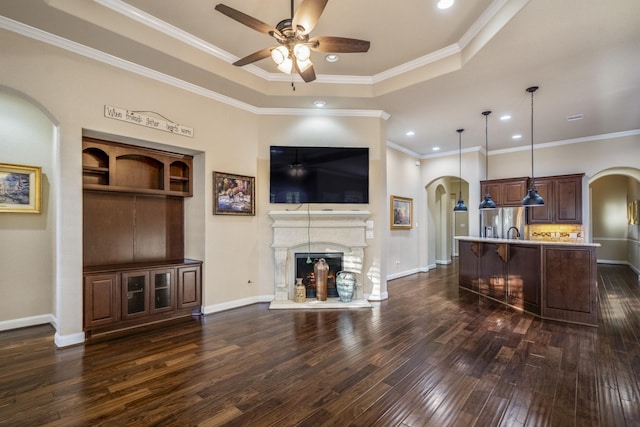 living area with arched walkways, dark wood-style floors, a fireplace with raised hearth, and a tray ceiling