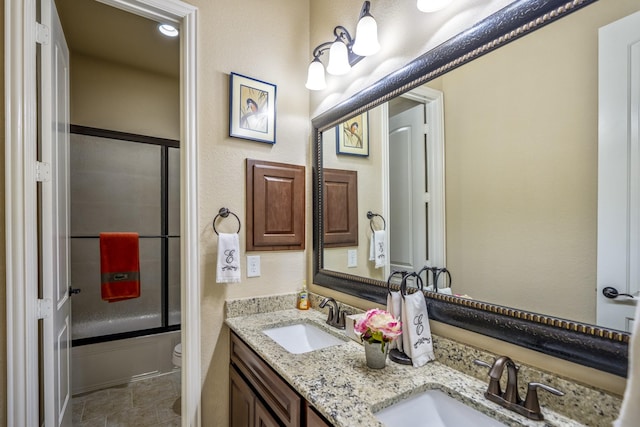 bathroom featuring double vanity, enclosed tub / shower combo, toilet, and a sink