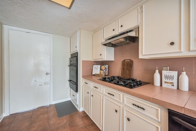 kitchen with backsplash, under cabinet range hood, tile countertops, a textured ceiling, and black appliances