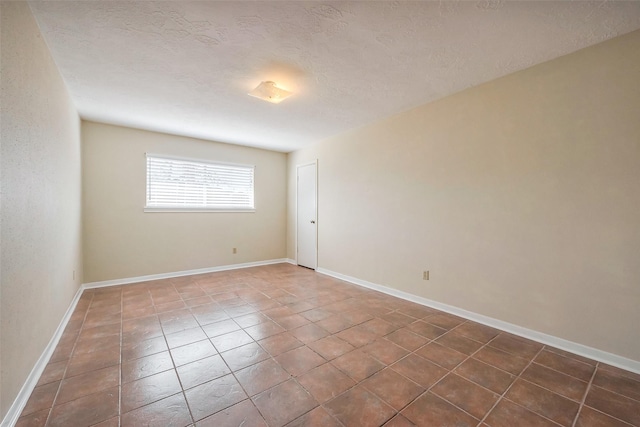 unfurnished room with dark tile patterned floors, baseboards, and a textured ceiling