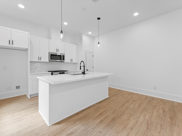 kitchen featuring stainless steel microwave, backsplash, a sink, light wood-type flooring, and range